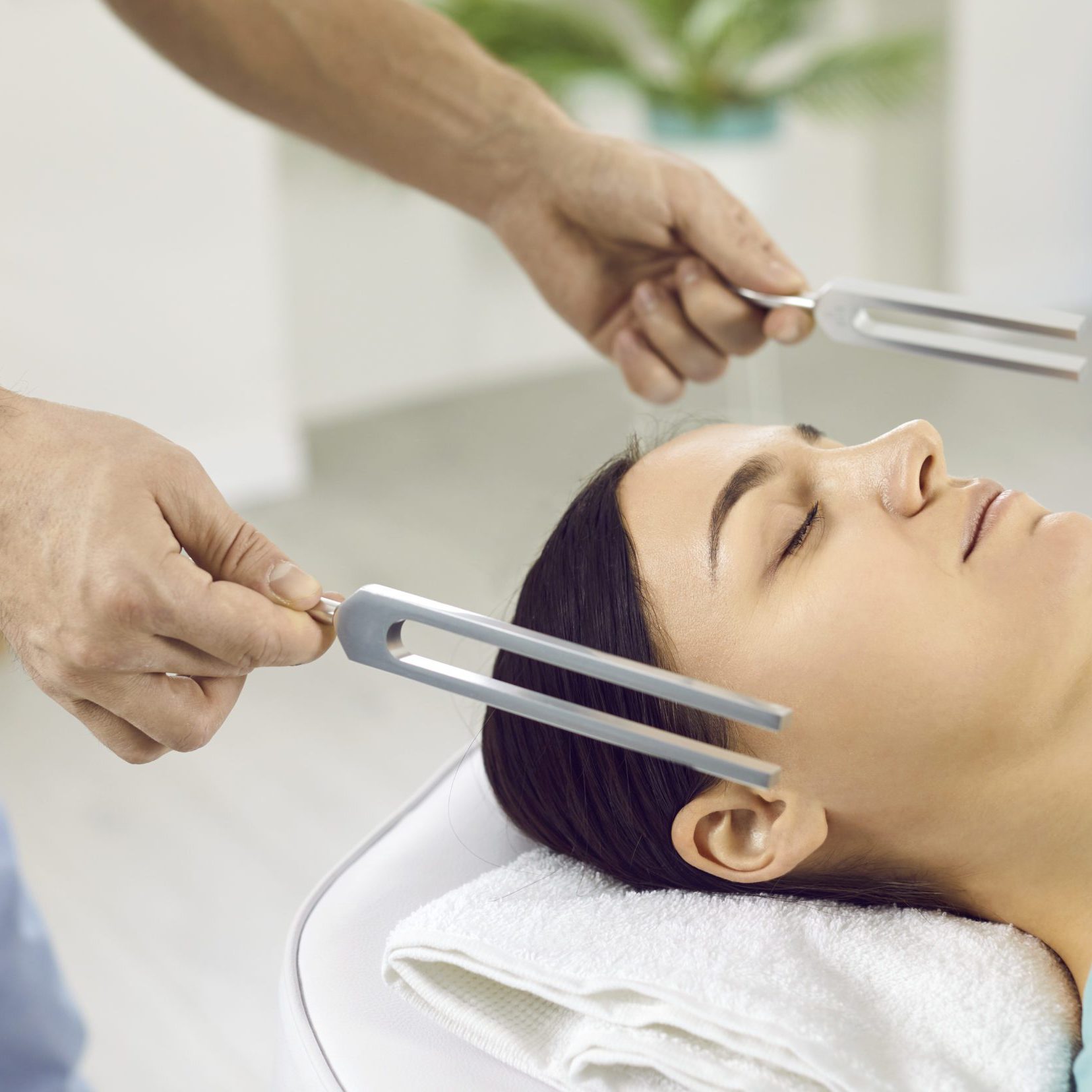 Holistic doctor healing young patient with help of tuning forks and sound therapy