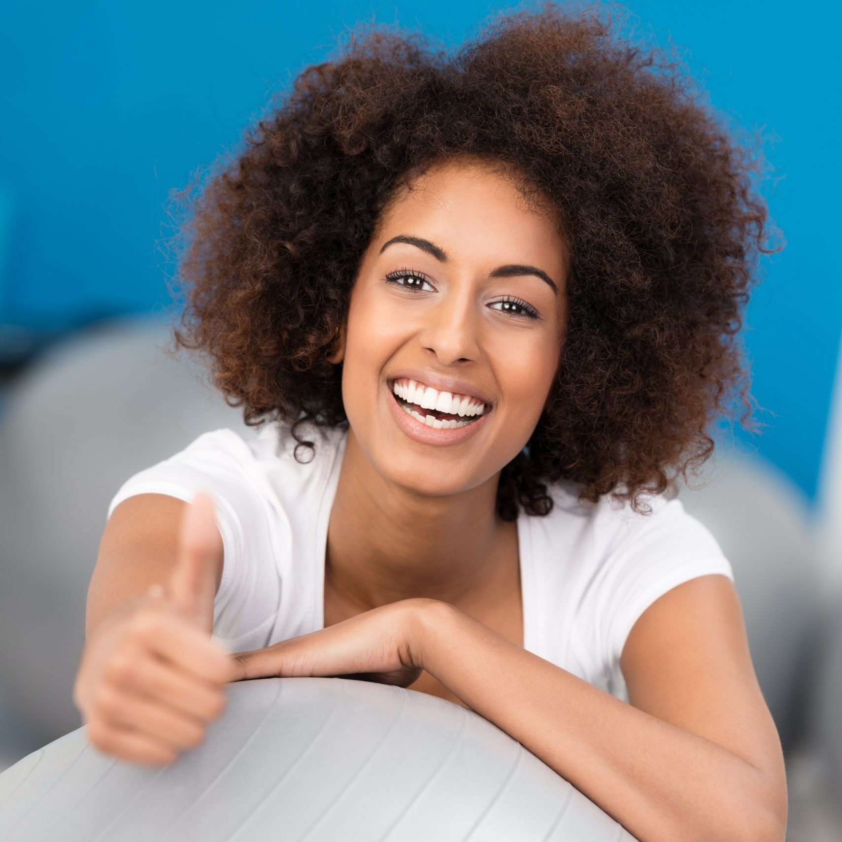 Laughing attractive African American woman with a wild afro hairstyle working out in a gym giving a thumbs up gesture of approval